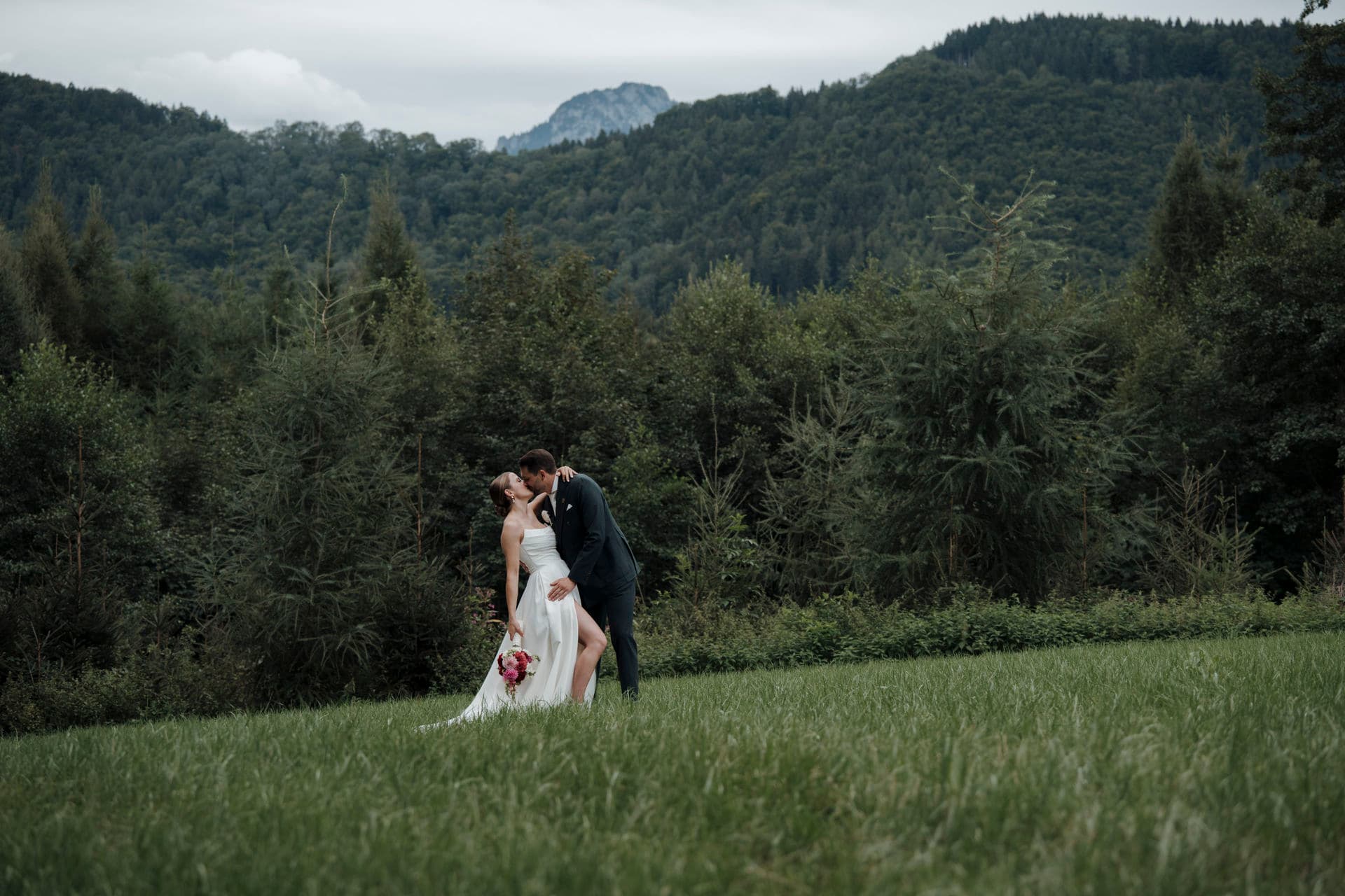 Brautpaar küsst sich in einer weiten Bergwiese, Braut im geblümten Kleid