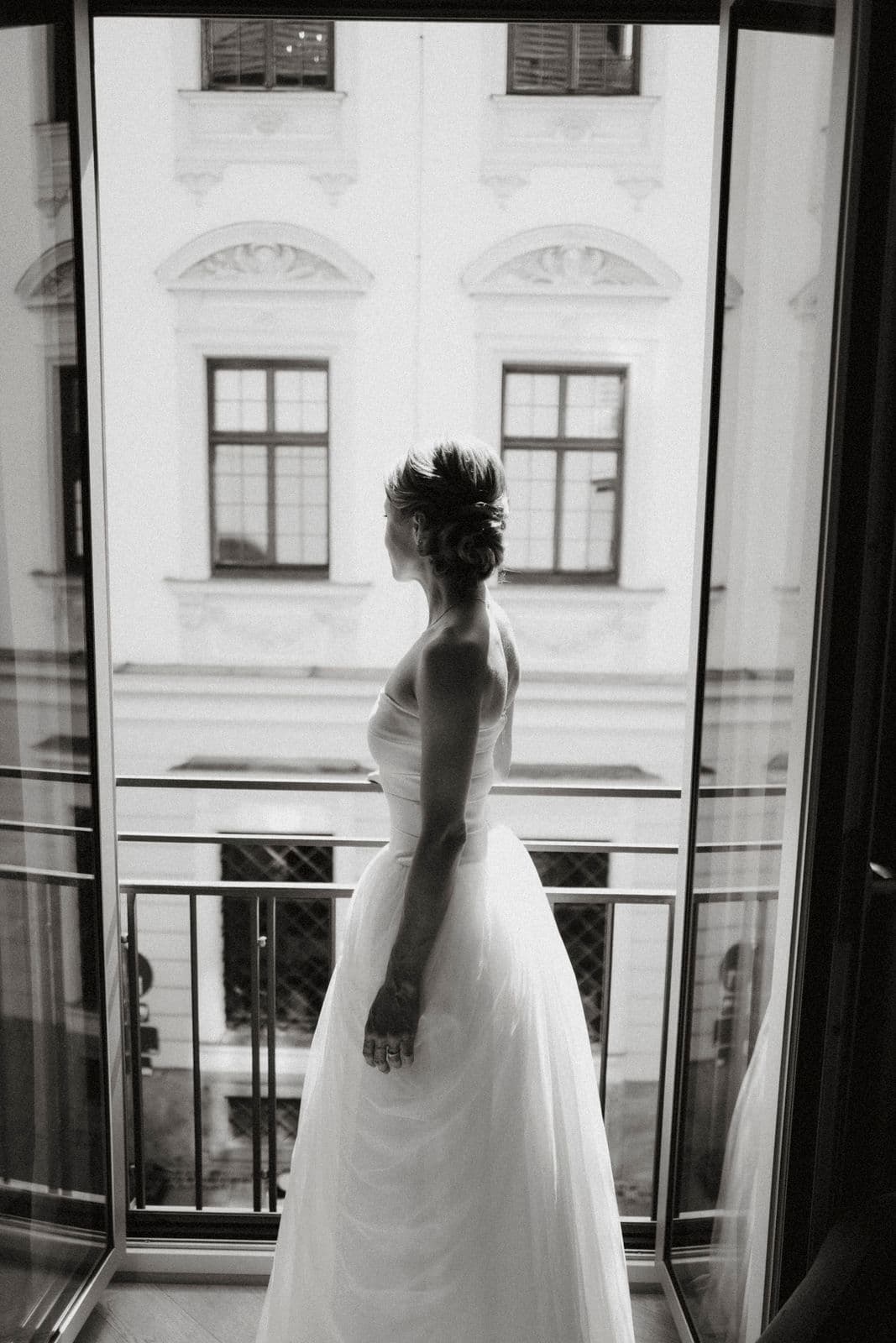 Braut am hohen Fenster mit Blick auf einen barocken Innenhof – Schwarz-Weiß