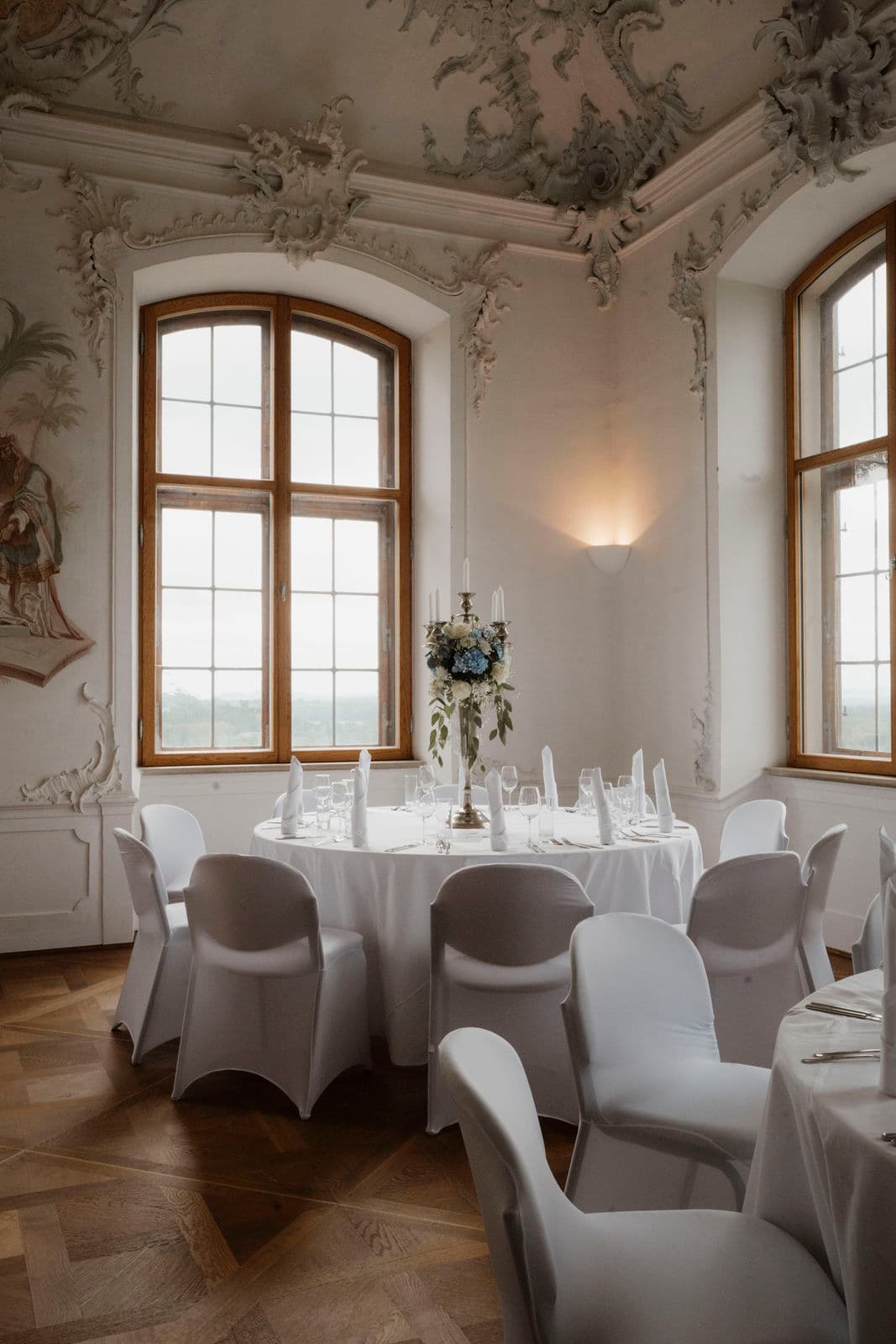 Elegant eingedeckte Tafel in einem verzierten Saal mit Rundbogenfenstern