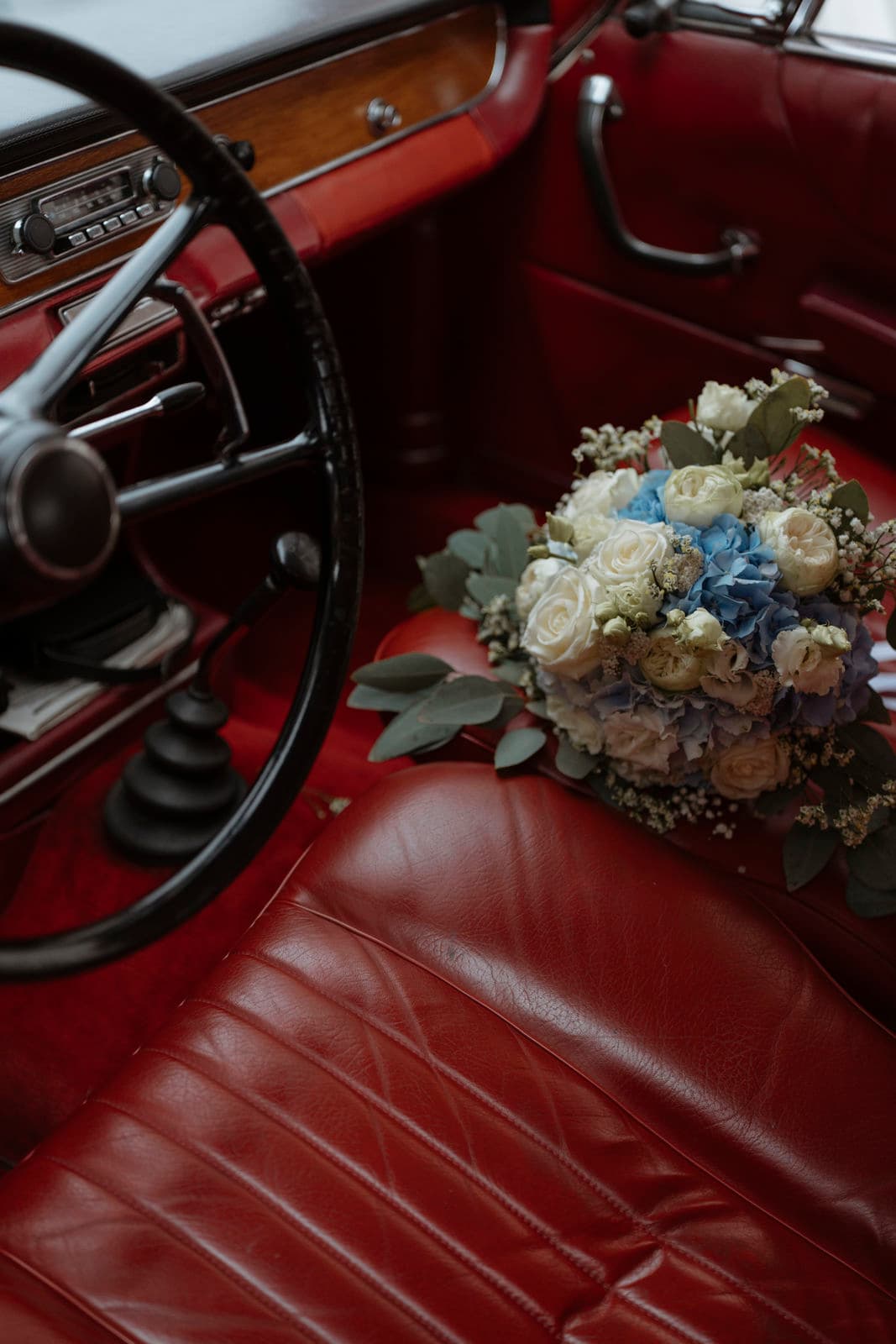 Blau-weißer Brautstrauß auf dem roten Ledersitz eines Oldtimers – Detail