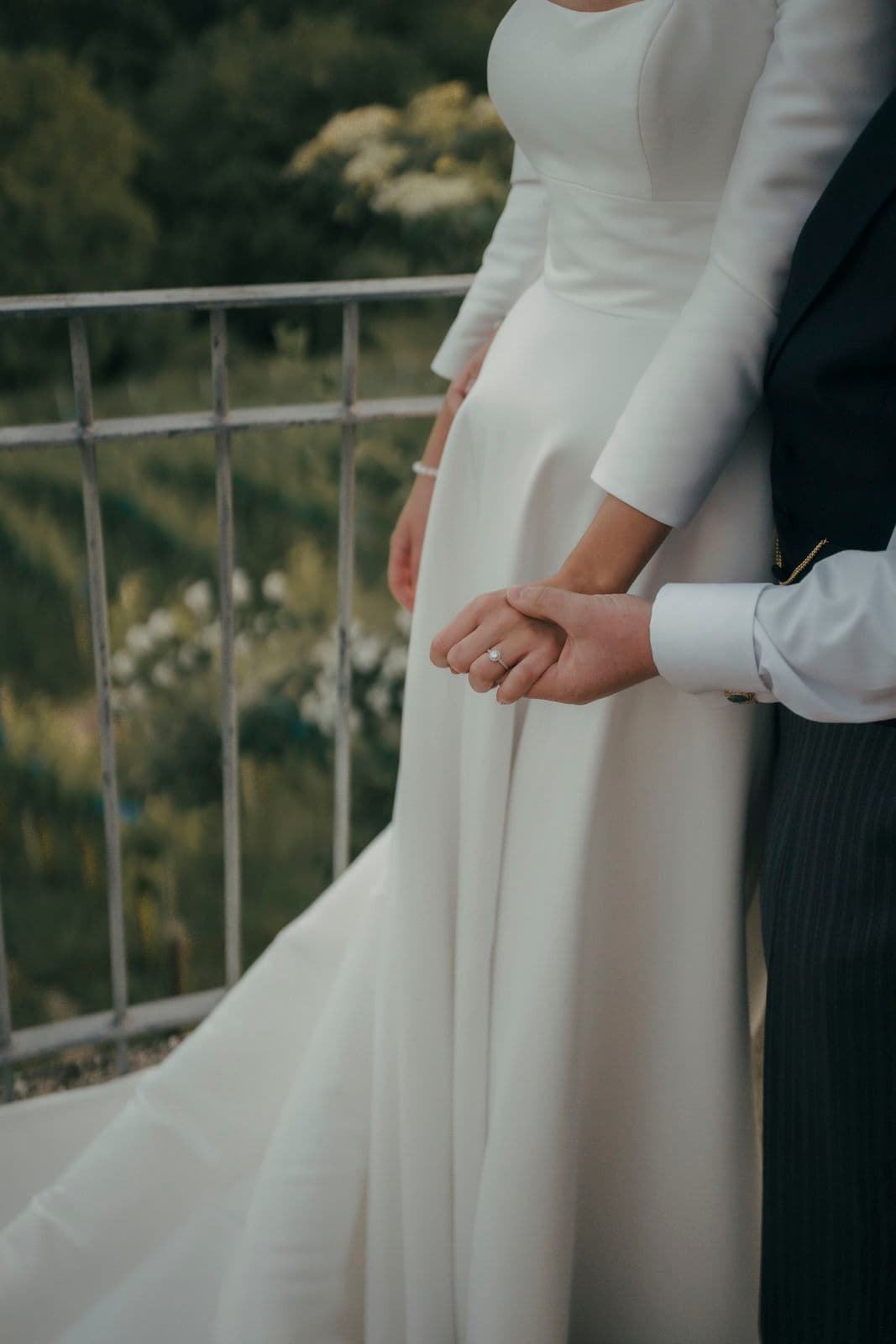 Braut im langärmeligen Kleid hält die Hand des Bräutigams am Geländer – Detail