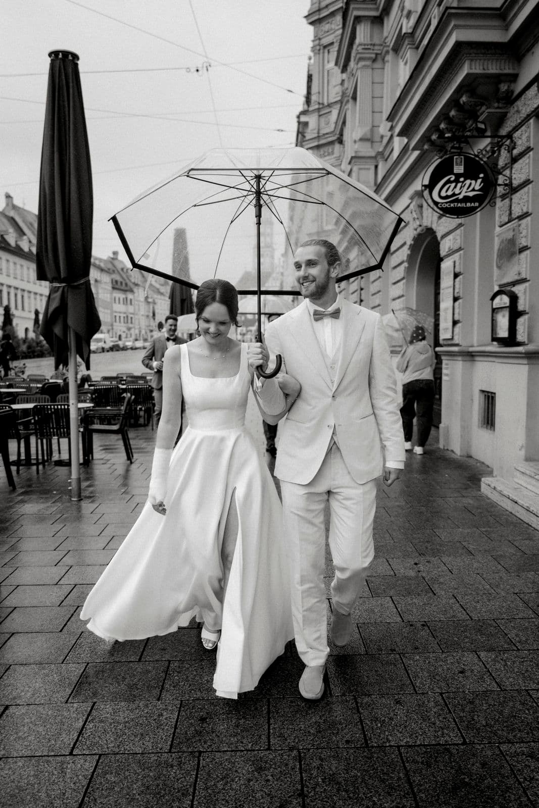 Braut und Bräutigam schlendern Arm in Arm unter dem Regenschirm an der Cocktailbar vorbei – Schwarz-Weiß