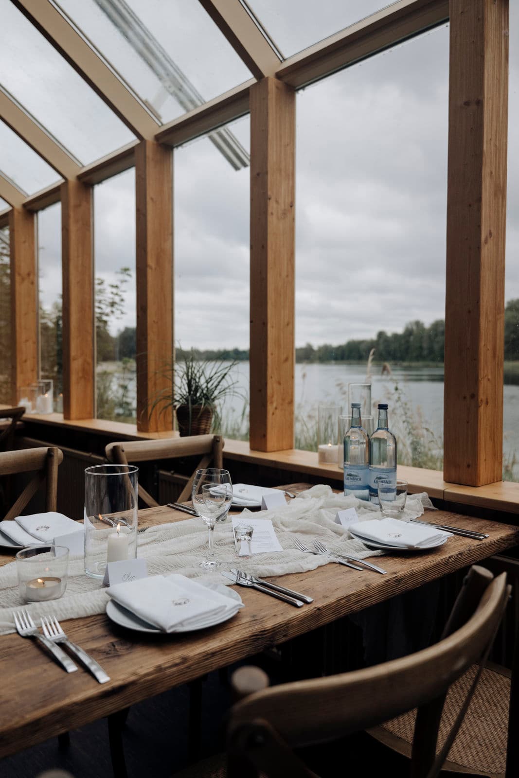 Festlich gedeckte Holztafel im Wintergarten mit Kerzen und Panoramablick auf den See