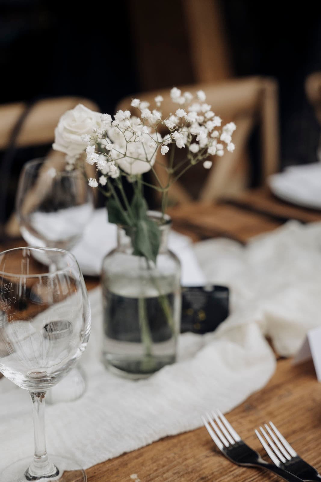 Schleierkraut und weiße Rose in der Glasvase auf dem Leinenläufer der Hochzeitstafel