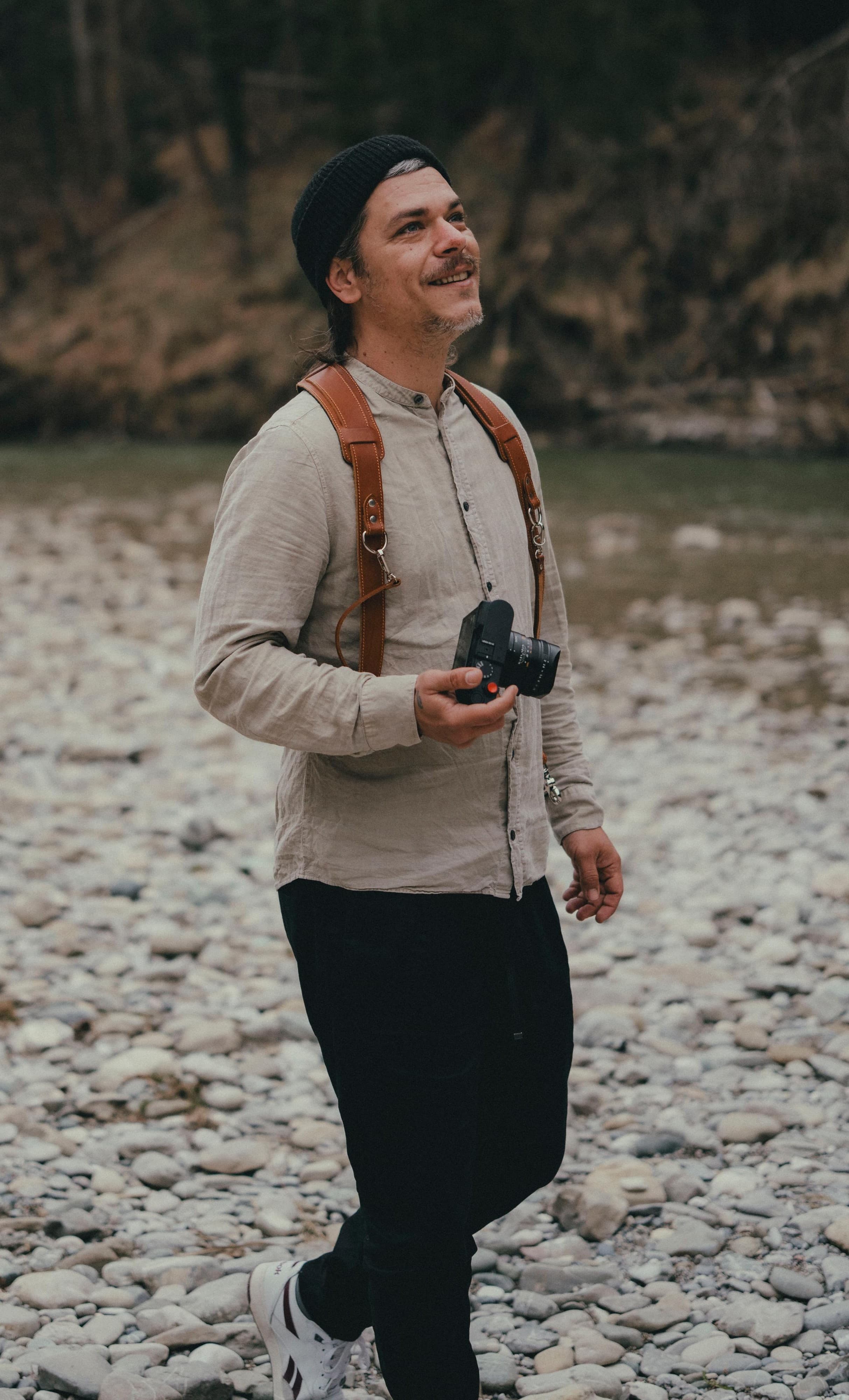Marc Gaedicke mit Kamera am Flussufer, lächelnd – Porträt des Hochzeitsfotografen